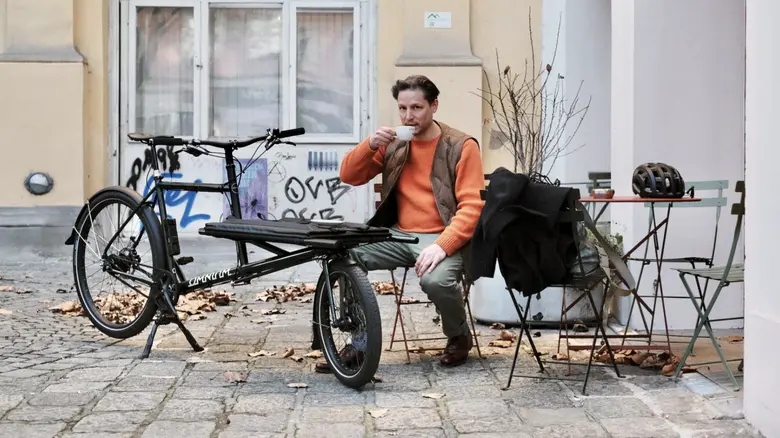 Mann sitzt neben Cargovelo und trinkt Kaffee